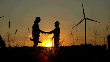 Silhouette of engineer and worker shaking hands on wind turbine background video