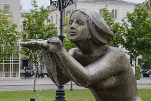 Statue of kneeling woman in the fountain. Water flowing from the hands of the statue photo