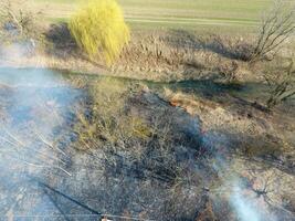 ardiente seco césped a lo largo el irrigación canal. fumar y el fuego de seco césped. quemado seco césped. foto