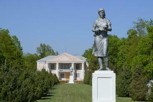 Statue of a collective farmer on a pedestal. The legacy of the Soviet era. A flower bed with tulips and young trees in the village of Oktyabrsky. Krasnodar Krai, Krasnoarmeisky District. photo