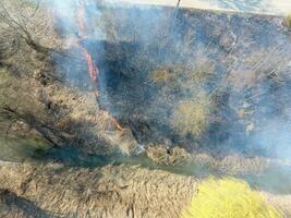 ardiente seco césped a lo largo el irrigación canal. fumar y el fuego de seco césped. quemado seco césped. foto