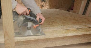 fermer de une ouvrier en utilisant une circulaire vu à Couper contre-plaqué. construction de une Nouveau en bois maison en utilisant Cadre technologie. video