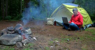 en man Arbetar på en bärbar dator i en turist läger i en skön skog. begrepp av frilansande, digital nomad eller avlägsen kontor. 4k video