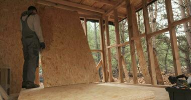 tijd vervallen van Mens arbeider gebouw houten kader huis. een timmerman montage houten osb paneel Aan de muur van toekomst huisje. Mens arbeider gebouw houten kader huis. timmerwerk en bouw concept. video