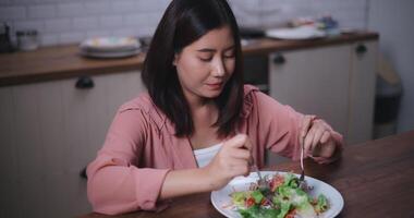 cenas do jovem ásia mulher comendo vegetal salada dentro cozinha às casa, saudável Comida e bem estar conceito video