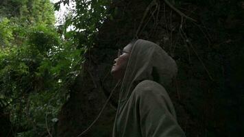 kvinna natur explorer ser runt om i de grön tropisk skog medan stående på skreva i de sten efter regn. ensam kvinna resande med djungel äventyr. utomhus- aktiviteter. solo- vandring. video