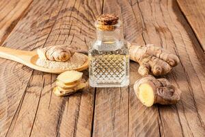 Homemade natural ginger root oil in bottle with a cork cap on a wooden background among ginger roots. Home Self-Care photo