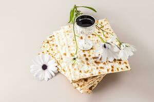 concepto de celebrando el judío fiesta de Pascua. un apilar de matza y un plata taza con rojo vino y un delicado flor. pastel antecedentes. foto