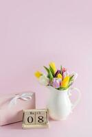 Beautiful still life for International Women's Day March. A jug with tulips, a gift box, a wooden calendar with a date. Vertical view. photo