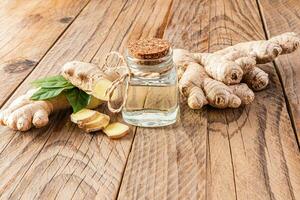 Bottle with cork cap with natural ginger root essential oil on the a large plant root on a wooden table. Concept of home oil preparation. photo