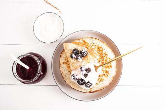 Top view of a large ceramic plate with crepes with sour cream and fresh berries. a jar of raspberry jam, a bowl of sour cream. still life. photo