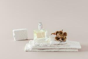 A chic bottle of perfume or eau de toilette on a podium made of white brick slices with a dried flower. A copy of the space. Pastel background. photo