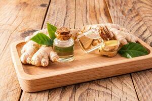 Two glass bottles with a cork cap with natural organic ginger root oil on a wooden tray among ginger roots. Tonic product. photo