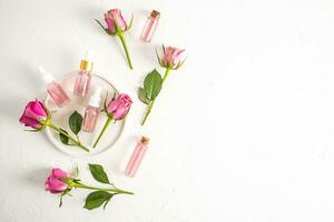 conjunto de diferente botellas con Rosa aceite, agua, suero establecido en Rosa pétalo petróleo en un yeso bandeja y blanco antecedentes. parte superior vista. plano poner. un Copiar espacio. foto