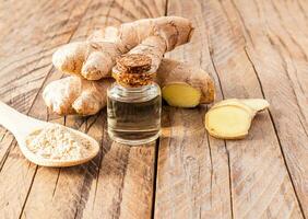 Ginger root essential oil in a glass bottle with a cork cap on a wooden table with root . Skin rejuvenation, strengthening hair growth. photo