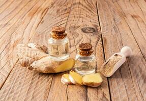 Homemade natural ginger root oil in two bottles with a cork cap on a wooden background among ginger roots. Home Self-Care. photo