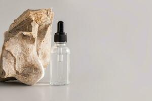 A serum for the care of dry skin of the face in a transparent bottle with a dropper on a gray background near a natural stone. mock-up. A copy space. photo