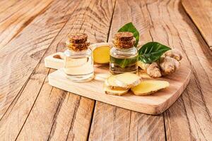 Natural homemade ginger root oil in two glass bottles with a cork cap on a wooden cutting board with ginger root slices. Multivitamins photo