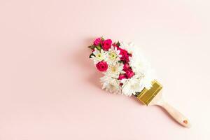 Paint brush with multicolored fresh flowers on pastel background. A copy space. Creative composition. Top view. Spring concept. photo