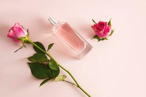 elegante botella de De las mujeres perfume o cosmético rociar en rosado antecedentes con delicado té cortar Rosa y capullo de rosa. parte superior vista. belleza y perfumería concepto. foto