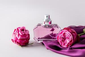 Glass elegant bottle of women's perfume among delicate rose buds and women's accessory chiffon purple scarf. Presentation of the fragrance. photo