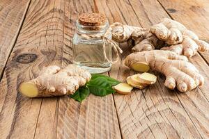 Bottle with cork cap with natural ginger root essential oil on the a large plant root on a wooden table. Concept of home oil preparation. photo