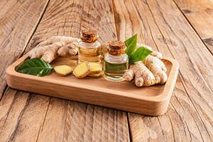 Natural ginger root oil in two glass bottles with cork cap on wooden tray and wooden table. Concept of home cooking of oil and home body care photo