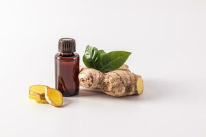Ginger root essential oil in a medical bottle with a cap on a white background with slices and root. Organic care concept. photo