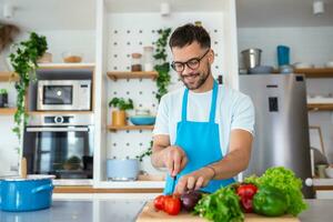 Handsome young man man stand at modern kitchen chop vegetables prepare fresh vegetable salad for dinner or lunch, young male cooking at home make breakfast follow healthy diet, vegetarian concept photo