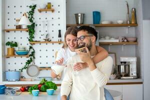 Portrait of happy young couple cooking together in the kitchen at home. Cute young couple enjoying their breakfast together she is pouring him milk photo