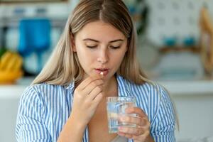 Millennial ill sick woman taking painkiller medicine to relieve stomachache pain sit on bed in the morning. Sick woman lying in bed with high fever. Cold flu and migraine. photo