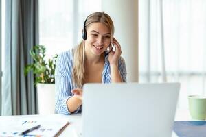 Happy young woman working on laptop while talking to customer on phone. Consulting corporate client in conversation with customer using computer. Service desk consultant talking in a call center. photo