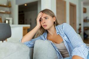 anxious worried woman sitting on couch at home. Frustrated confused female feels unhappy, problems in personal life, quarrel break up with boyfriend and unexpected pregnancy concept photo