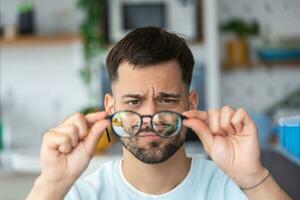 Young man holds glasses with diopter lenses and looks through them, the problem of myopia, vision correction photo