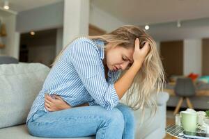 Woman in painful expression holding hands against belly suffering menstrual period pain, lying sad on home bed, having tummy cramp in female health concept photo