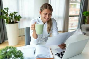 Doctor professional female doctor wearing uniform taking notes in medical journal, filling documents, patient illness history, looking at laptop screen, student watching webinar photo