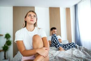 Frustrated sad girlfriend sit on bed think of relationship problems, thoughtful couple after quarrel lost in thoughts, upset lovers consider break up, offended person disappointed by boyfriend photo
