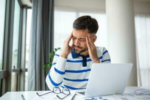 Businessman office working holding sore head pain from desk working and sitting all day using laptop computer or notebook suffering headache sick worker overworking concept photo
