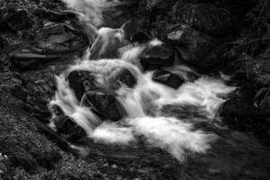 Black and white view of water stream between rocks. Close up photo