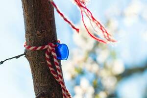 Martenitsa with blue heart shaped bead tied on the tree in focus photo