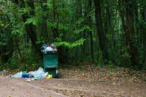 pile of garbage and a full trash bin in the forest. garbage pollution concept photo