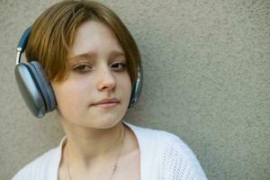 Portrait of a teenage girl in headphones against a gray wall. photo