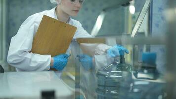 scientist worker checking the quality of water bottles on the machine conveyor line at the industrial factory. Female worker recording data at the beverages manufacturing line production. video