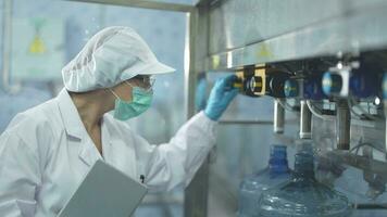 scientist worker checking the quality of water bottles on the machine conveyor line at the industrial factory. Female worker recording data at the beverages manufacturing line video