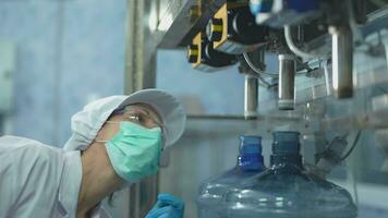 scientist worker checking the quality of water bottles on the machine conveyor line at the industrial factory. Female worker recording data at the beverages manufacturing line video