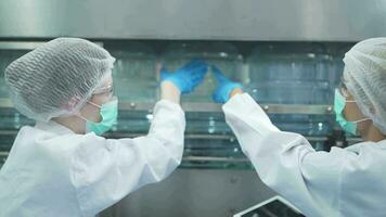 scientist worker checking the quality of water bottles on the machine conveyor line at the industrial factory. Female worker recording data at the beverages manufacturing line video