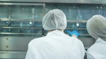 scientist worker checking the quality of water bottles on the machine conveyor line at the industrial factory. Female worker recording data at the beverages manufacturing line video