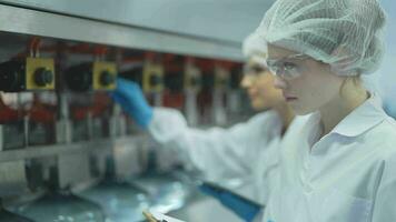 scientist worker checking the quality of water bottles on the machine conveyor line at the industrial factory. Female worker recording data at the beverages manufacturing line video