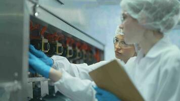 scientist worker checking the quality of water bottles on the machine conveyor line at the industrial factory. Female worker recording data at the beverages manufacturing line video