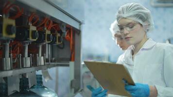 scientist worker checking the quality of water bottles on the machine conveyor line at the industrial factory. Female worker recording data at the beverages manufacturing line video